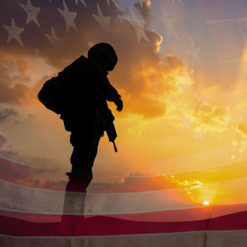 Silhouette of a soldier in front of an American flag at sunset